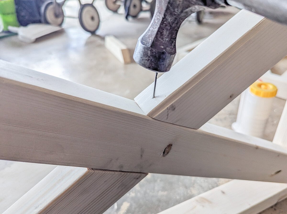 securing X in chair side with a hammer and finishing nail.